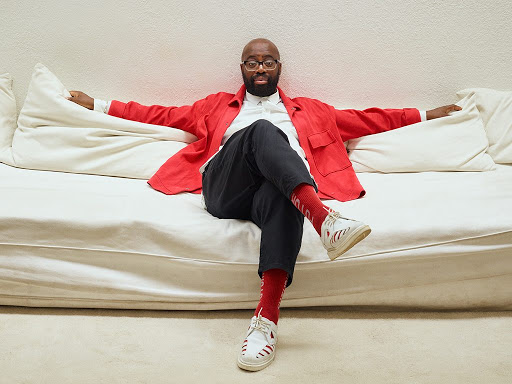 A man in a red shirt sits on a white sofa with his arms stretched out